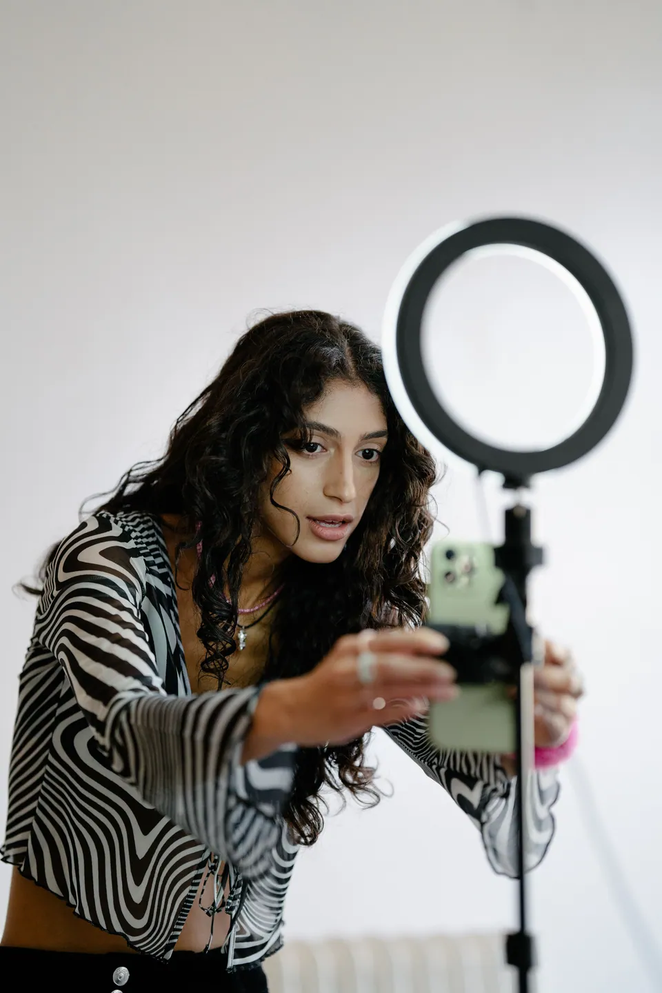 Woman adjusting a phone mounted on a ring-light tripod
