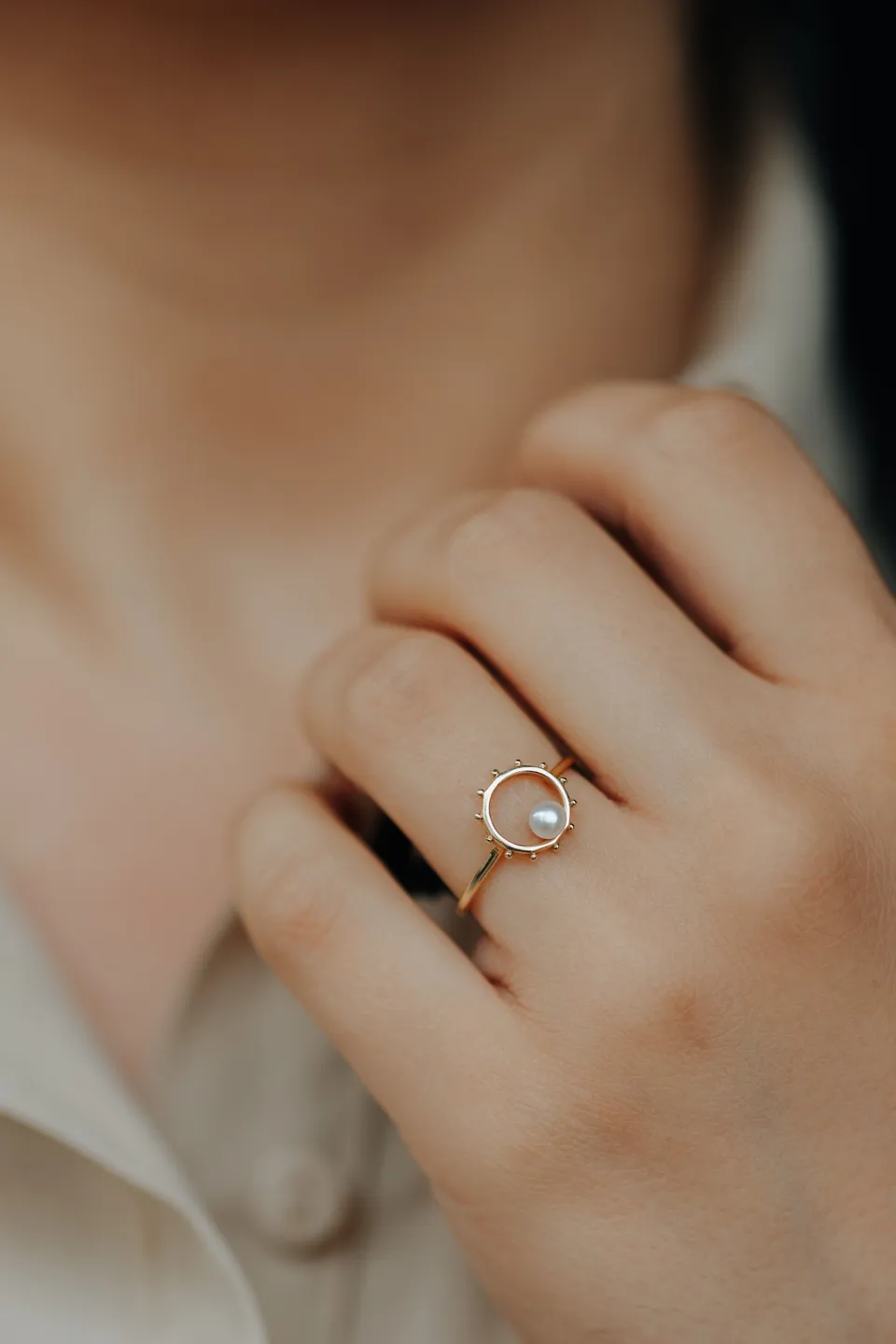 Close view of a hand wearing a gold ring with a pearl