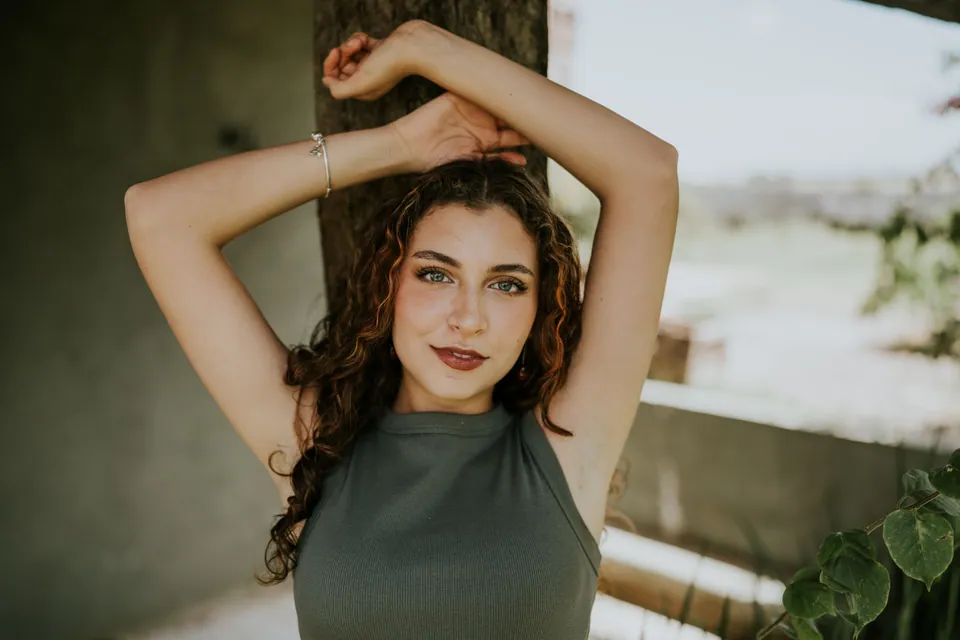 Woman raising her arms in sunlight beside a shaded wall