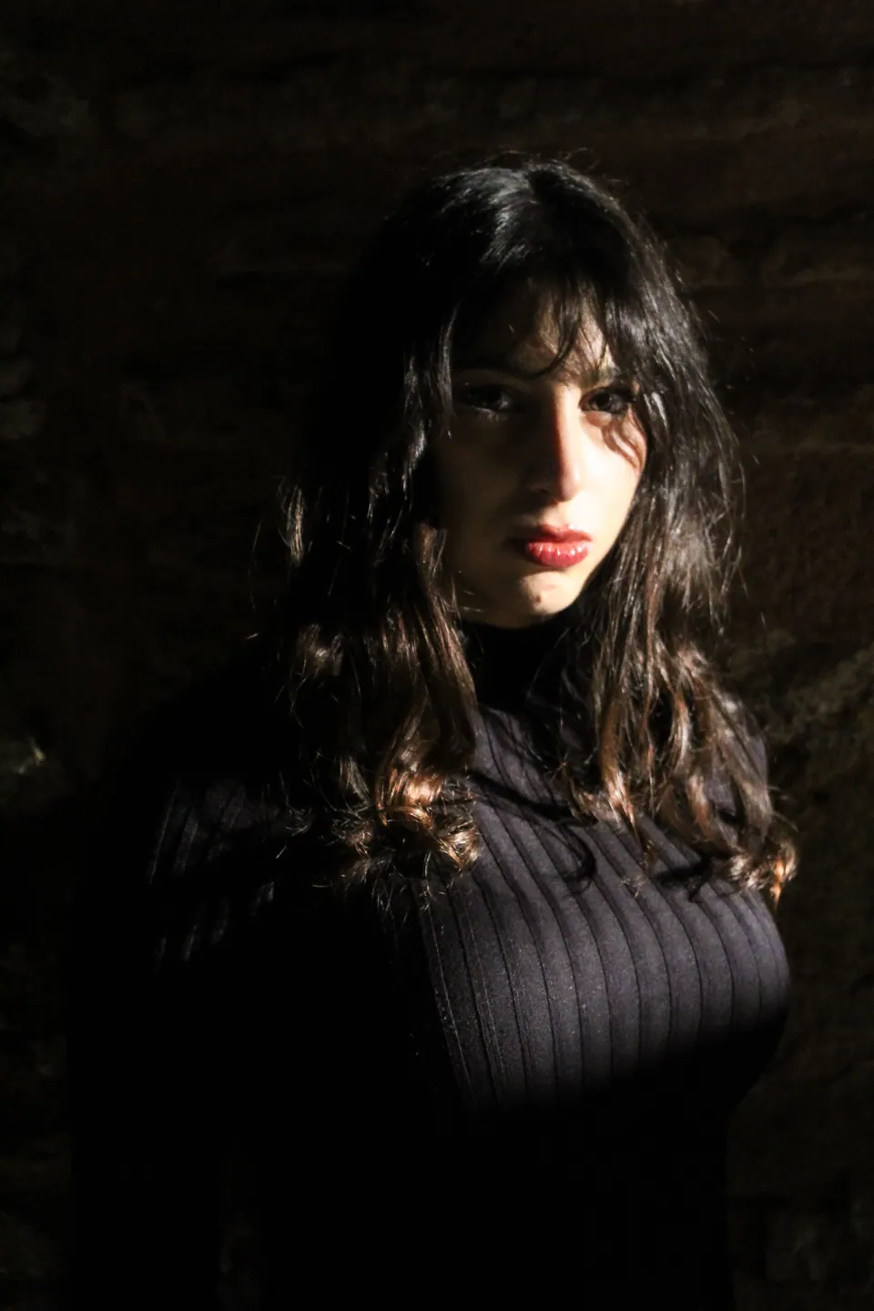 Portrait of a woman with bright light across one side of her face and deep shadows around her