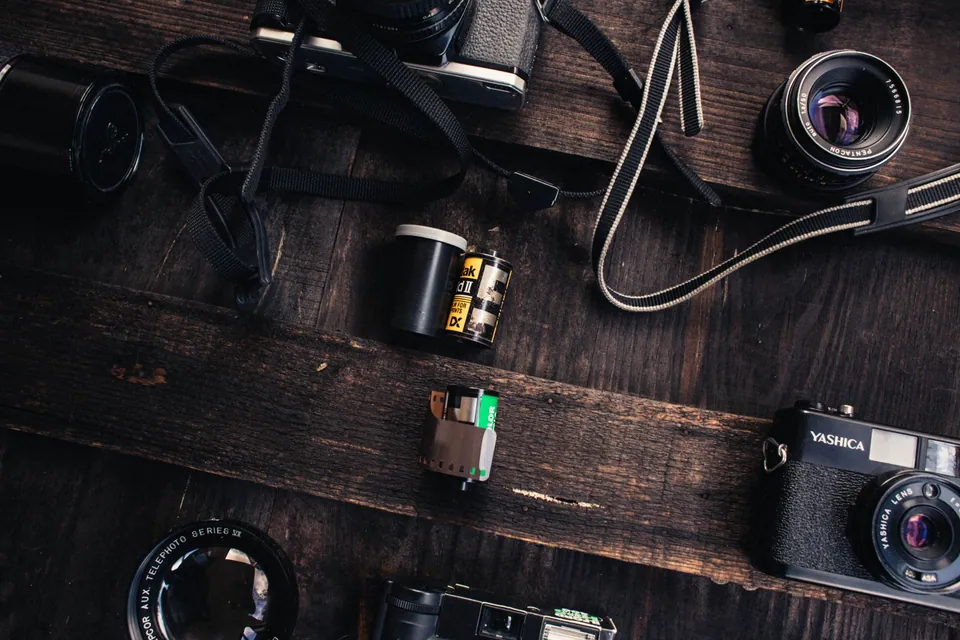 Film cameras, lenses, and film rolls on a wooden table