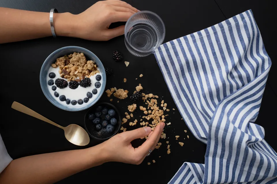 Overhead view of granola, blueberries and a bowl of yogurt on a dark table